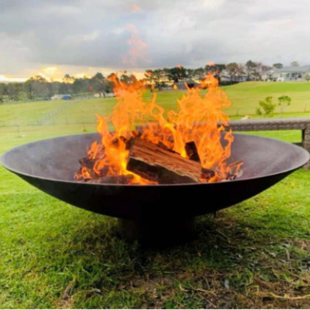 1200mm cast iron Fire pit with flames burning on a grassy field
