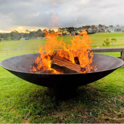 1200mm cast iron Fire pit with flames burning on a grassy field