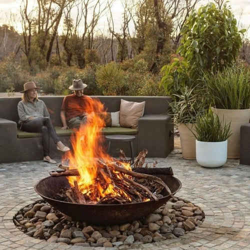 Two people sitting on a patio with a 1500mm cast iron fire pit and outdoor furniture.