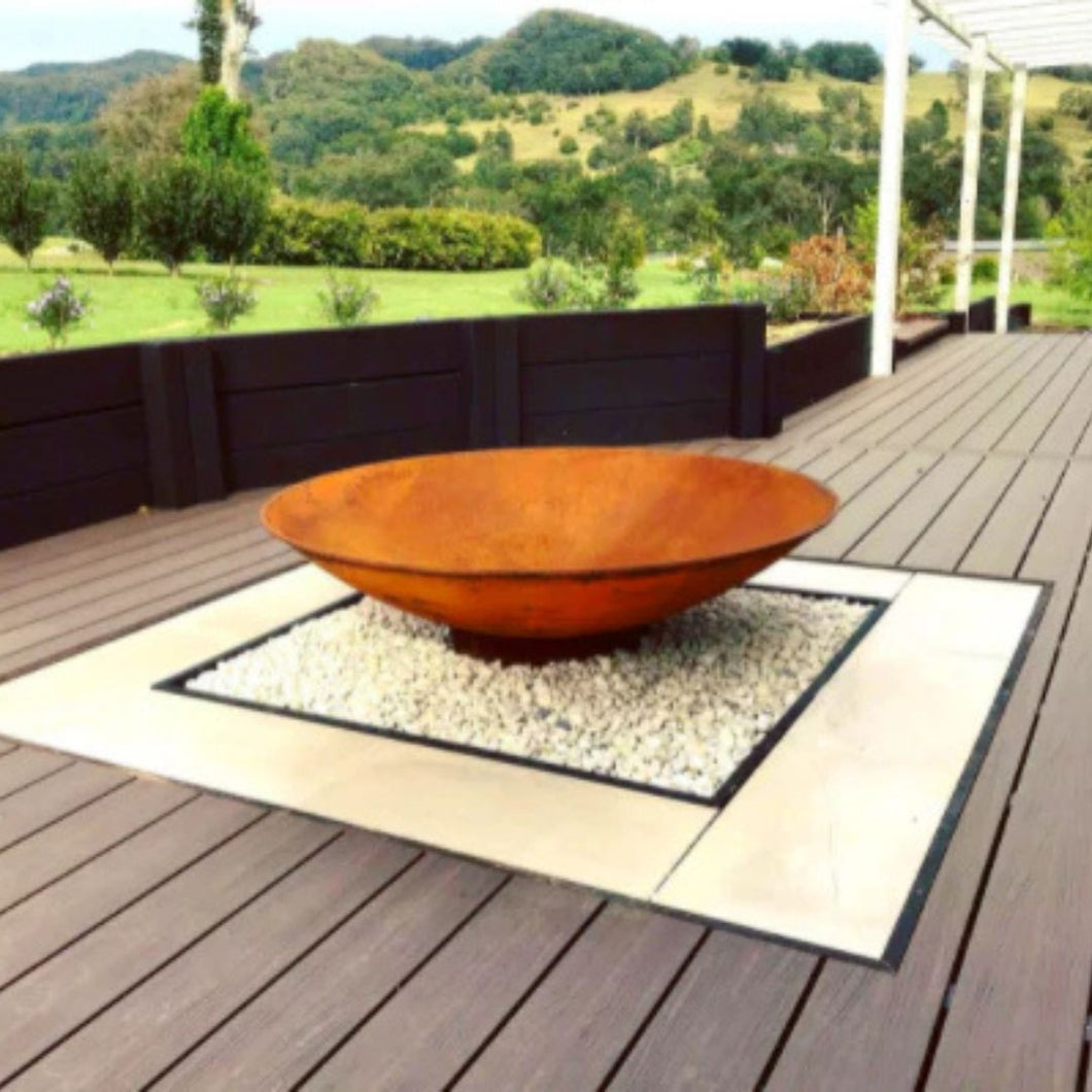 Rust-colored cast iron fire pit on a wooden deck with a scenic background