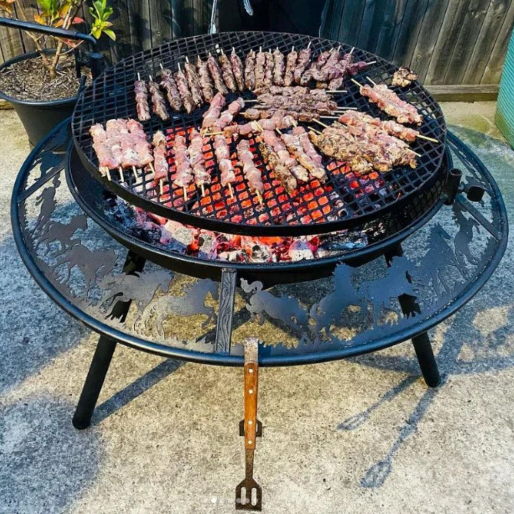 900mm BBQ fire pit with skewers of food on a patio