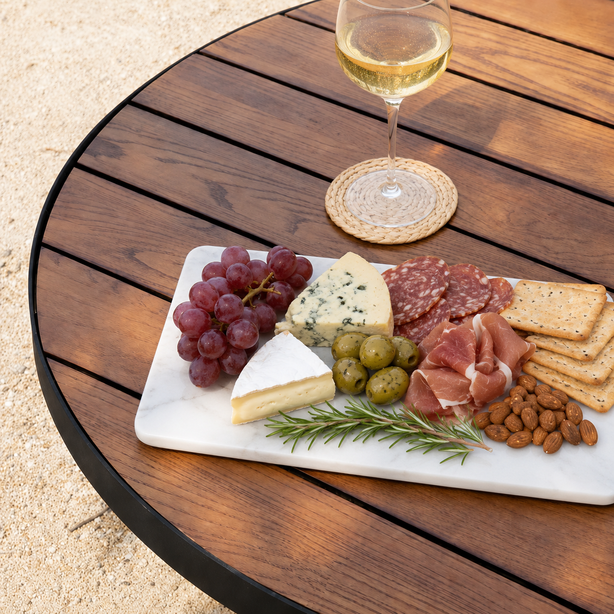 Platter of assorted meats, cheeses, and fruits on a Solid Merbau Timber Fire Pit Table Top with a glass of white wine.