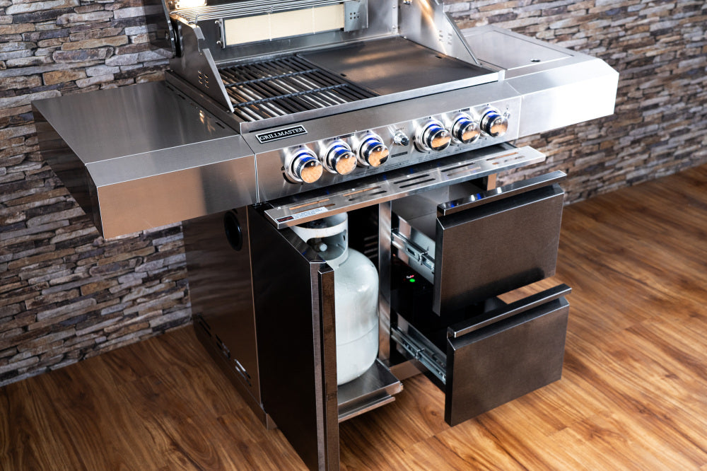 Stainless steel outdoor grill with gas bottle against a stone wall.