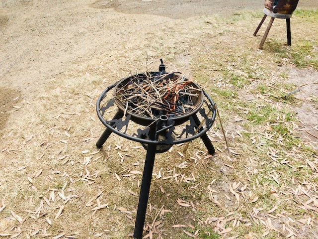 Black metal fire pit with twigs on a grassy area
