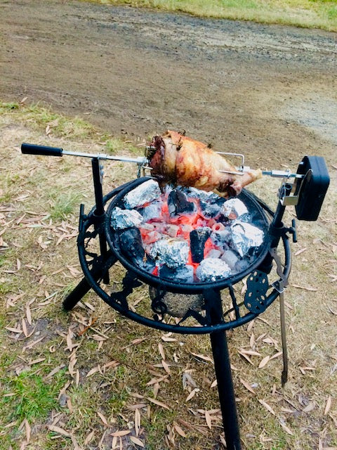 Rotisserie grill with a roasted chicken over an open flame outdoors.