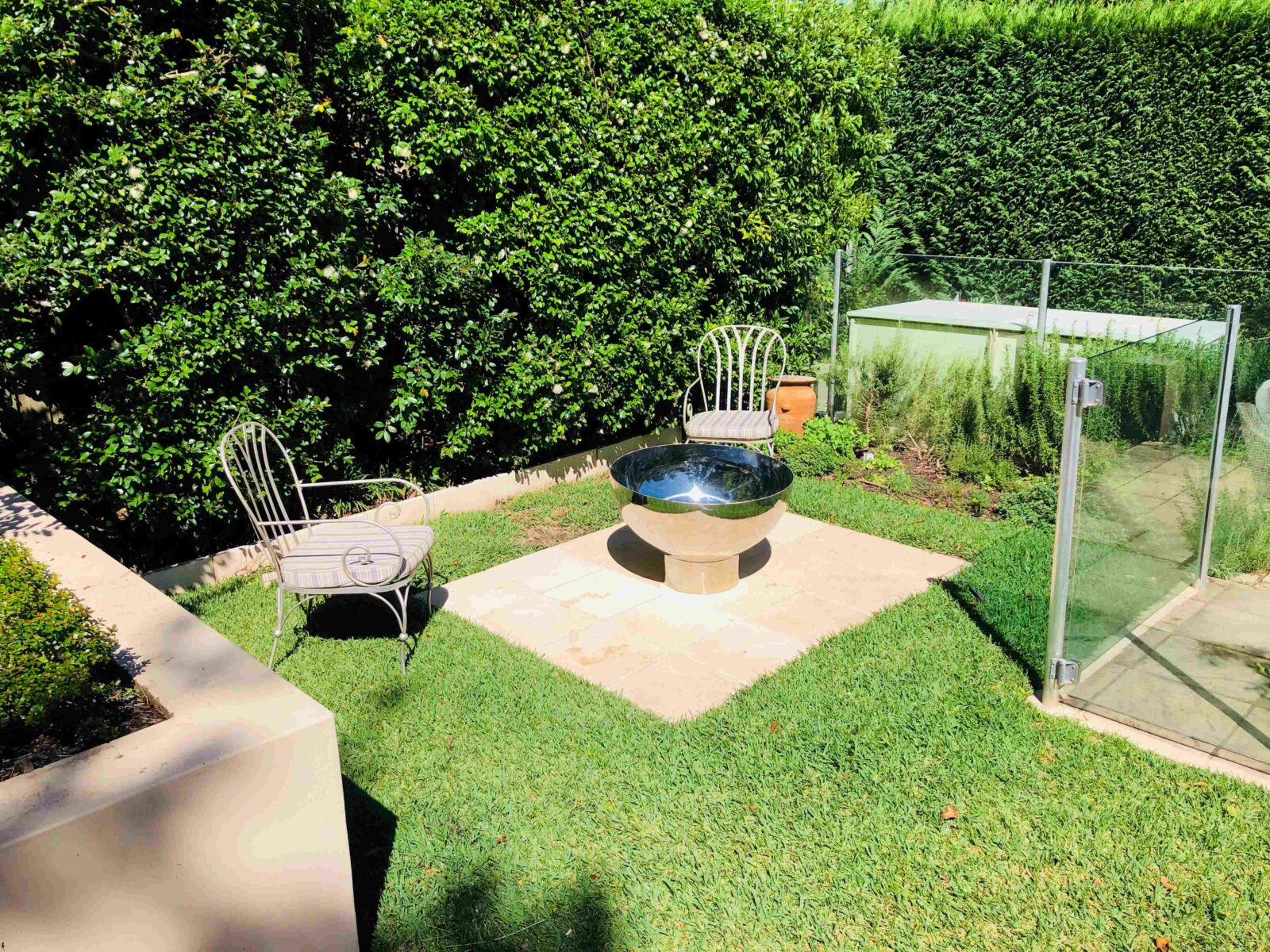 Garden with stainless steel fire pit, chairs, and a glass-enclosed area.
