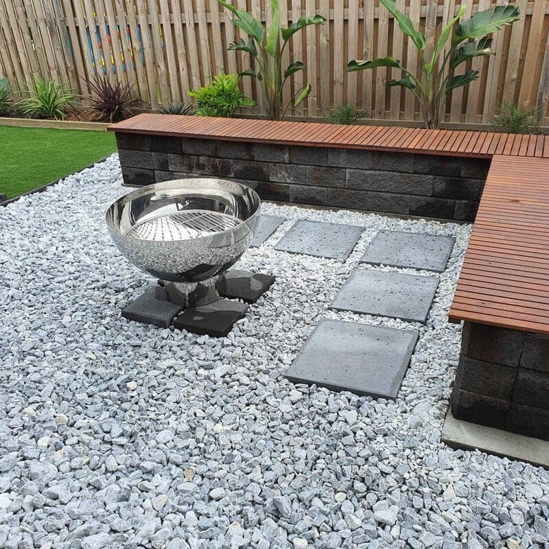 Outdoor garden setting with a fire pit, stone pathway, and wooden bench.