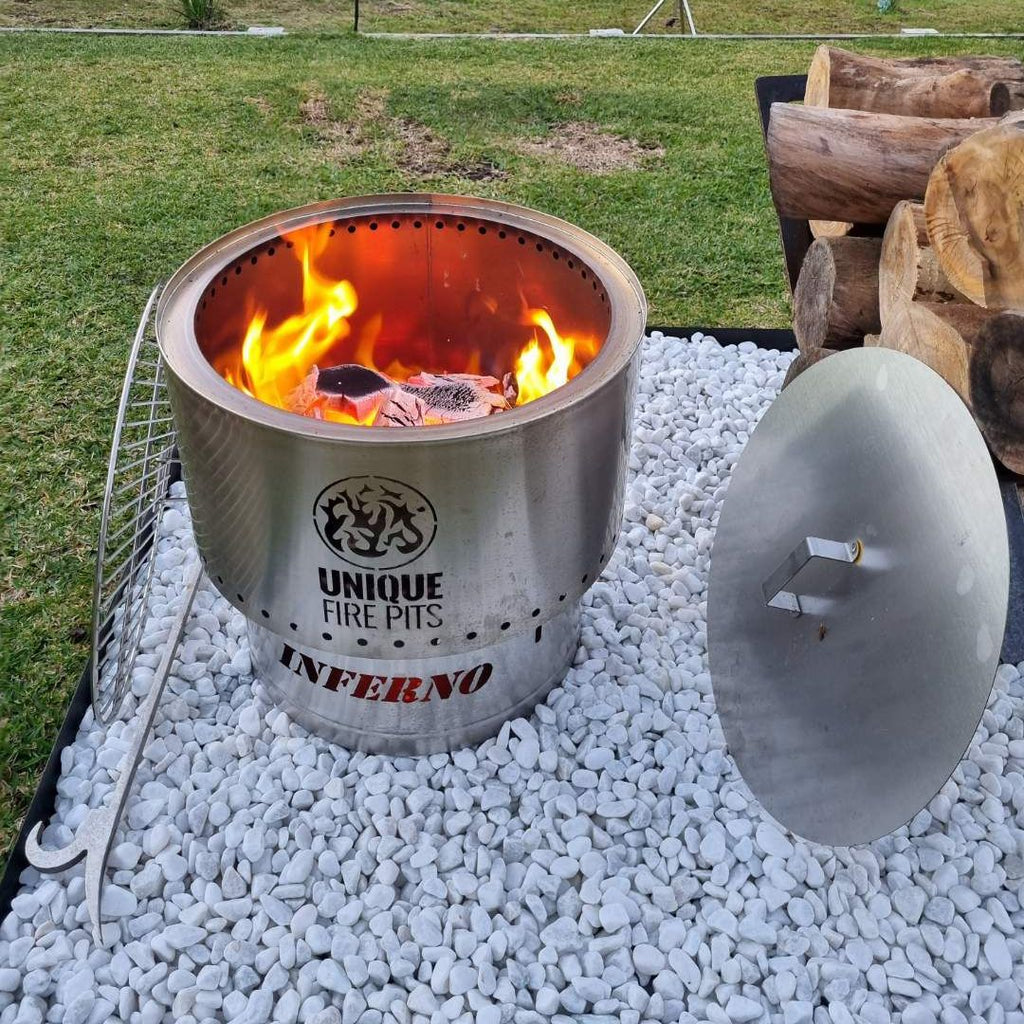 smokeless fire pit with flames on a bed of white stones, surrounded by logs and tools.