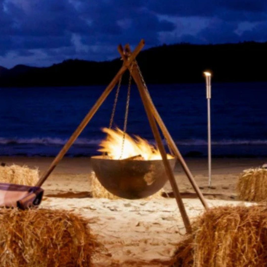 Tripod fire pit on a beach at night with hay bales and ocean view