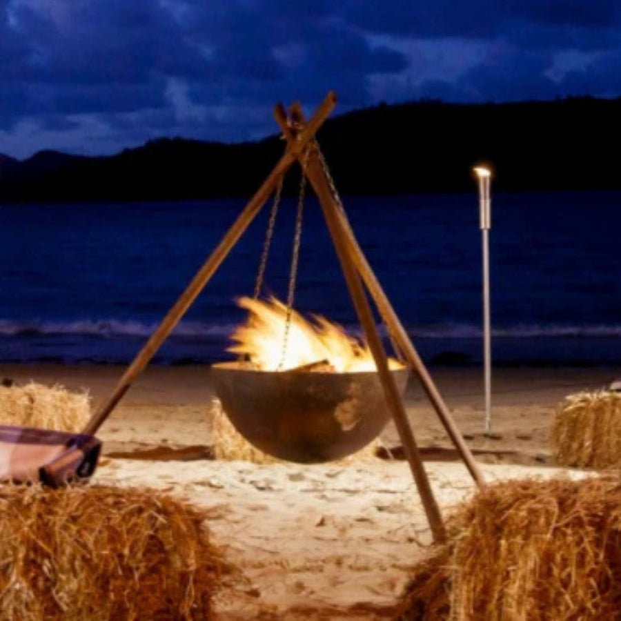 Tripod fire pit on a beach at night with hay bales and ocean view